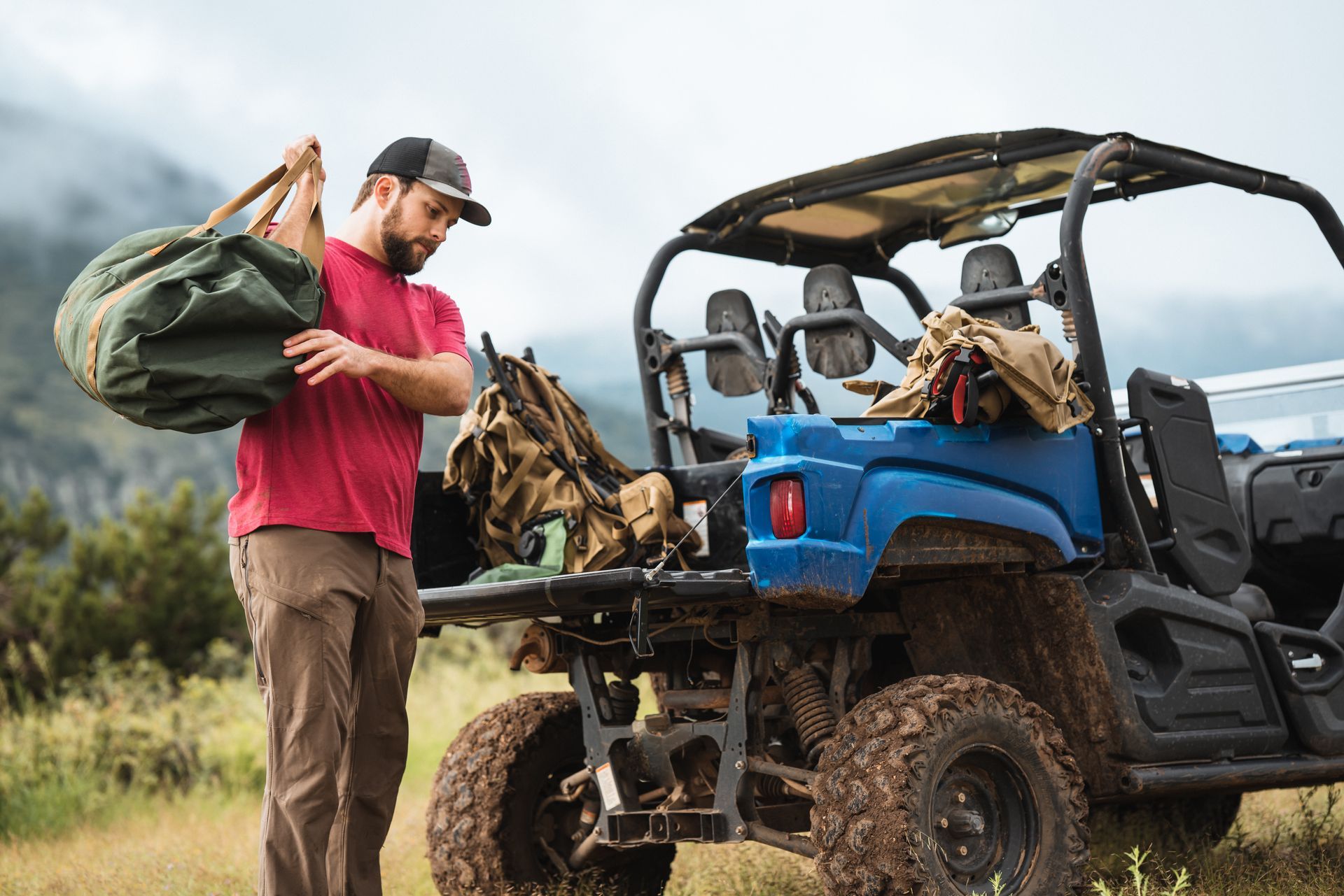 Man loading gear into a blue off-road vehicle in a muddy field