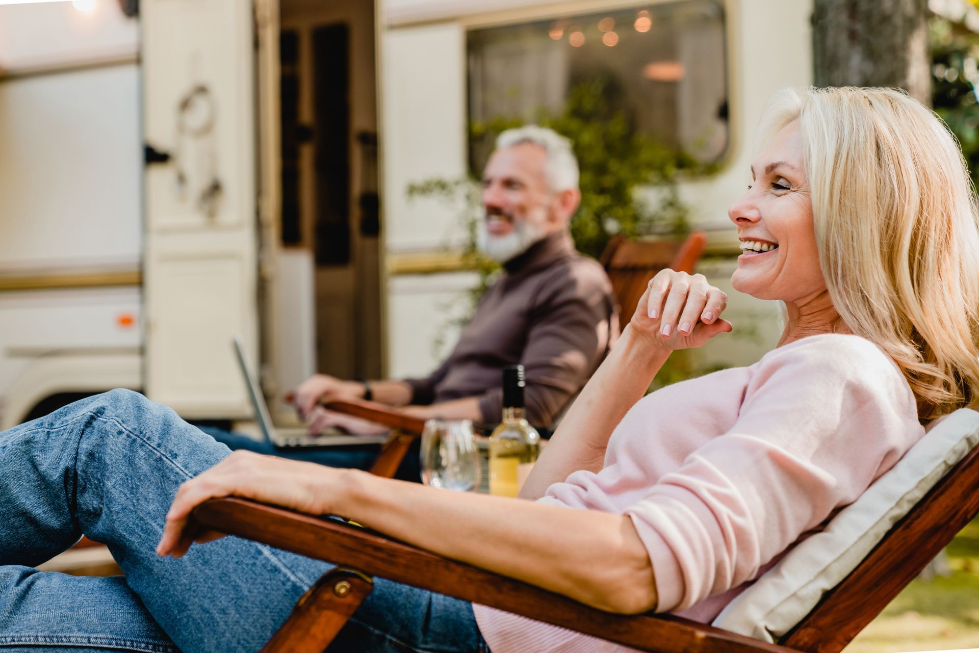 Two people relaxing in outdoor lounge chairs, smiling on a patio with drinks nearby.