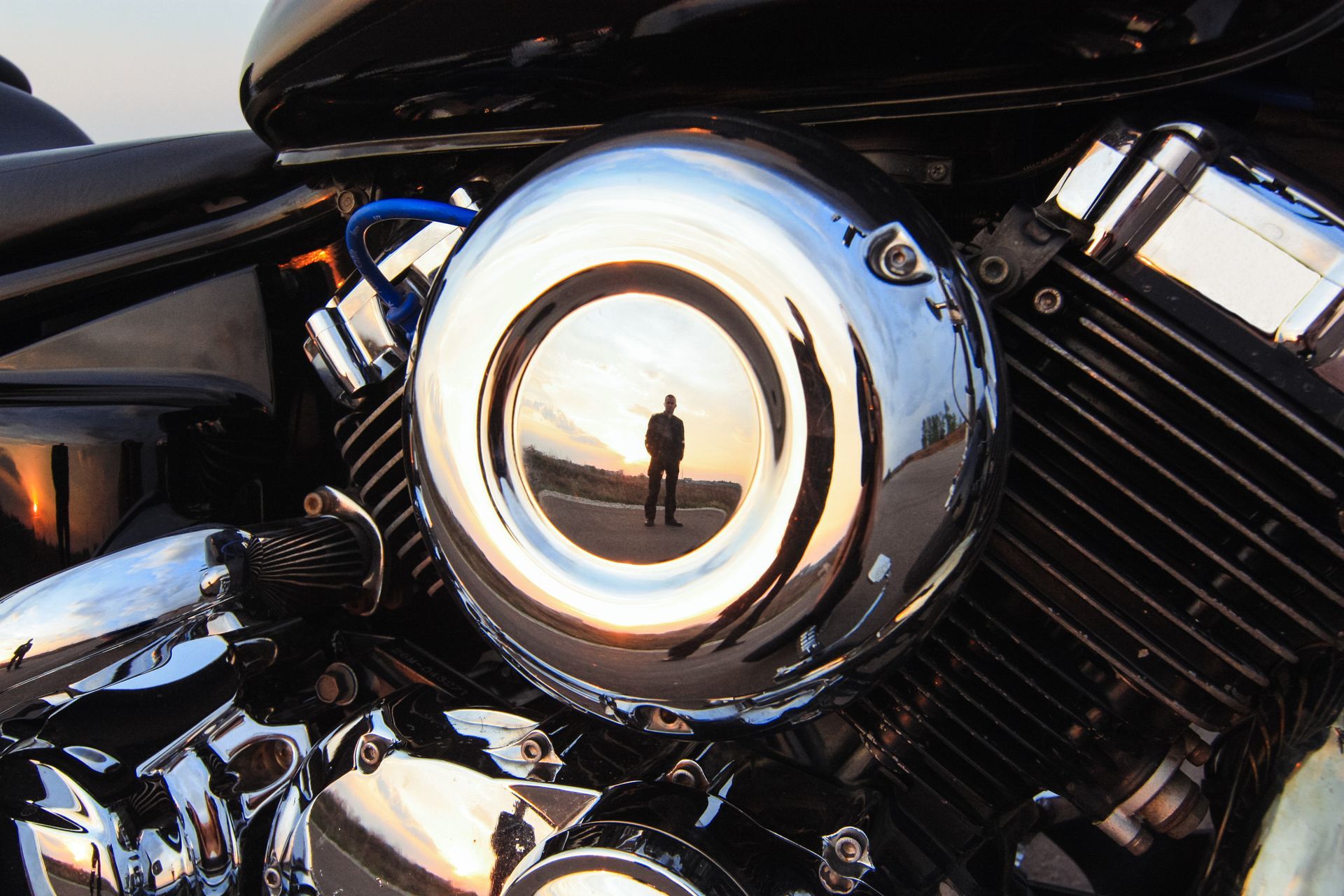 Chrome motorcycle headlight with a reflection of a standing person in a black jacket