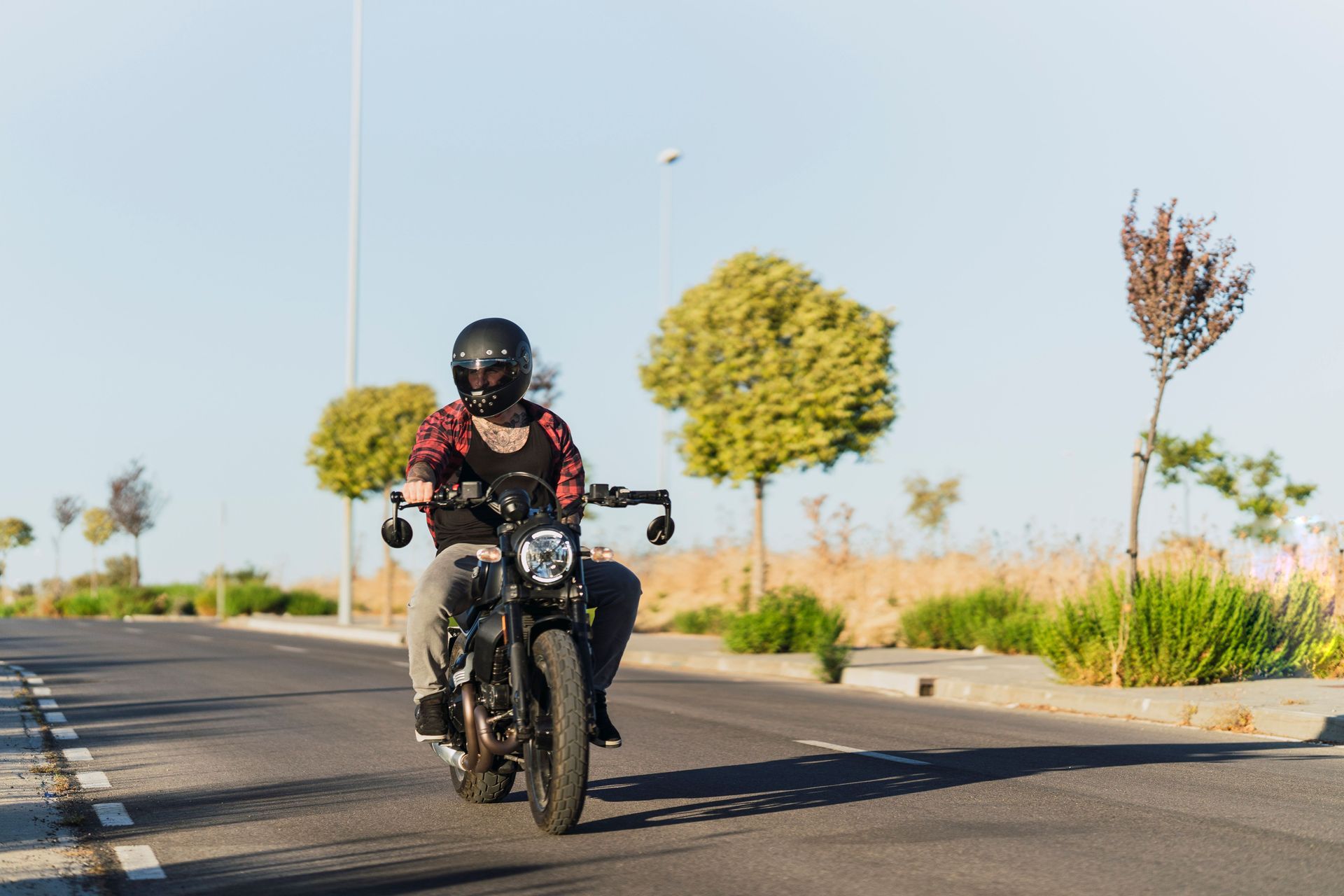 Motorcyclist riding on a sunlit road beside trees and shrubs