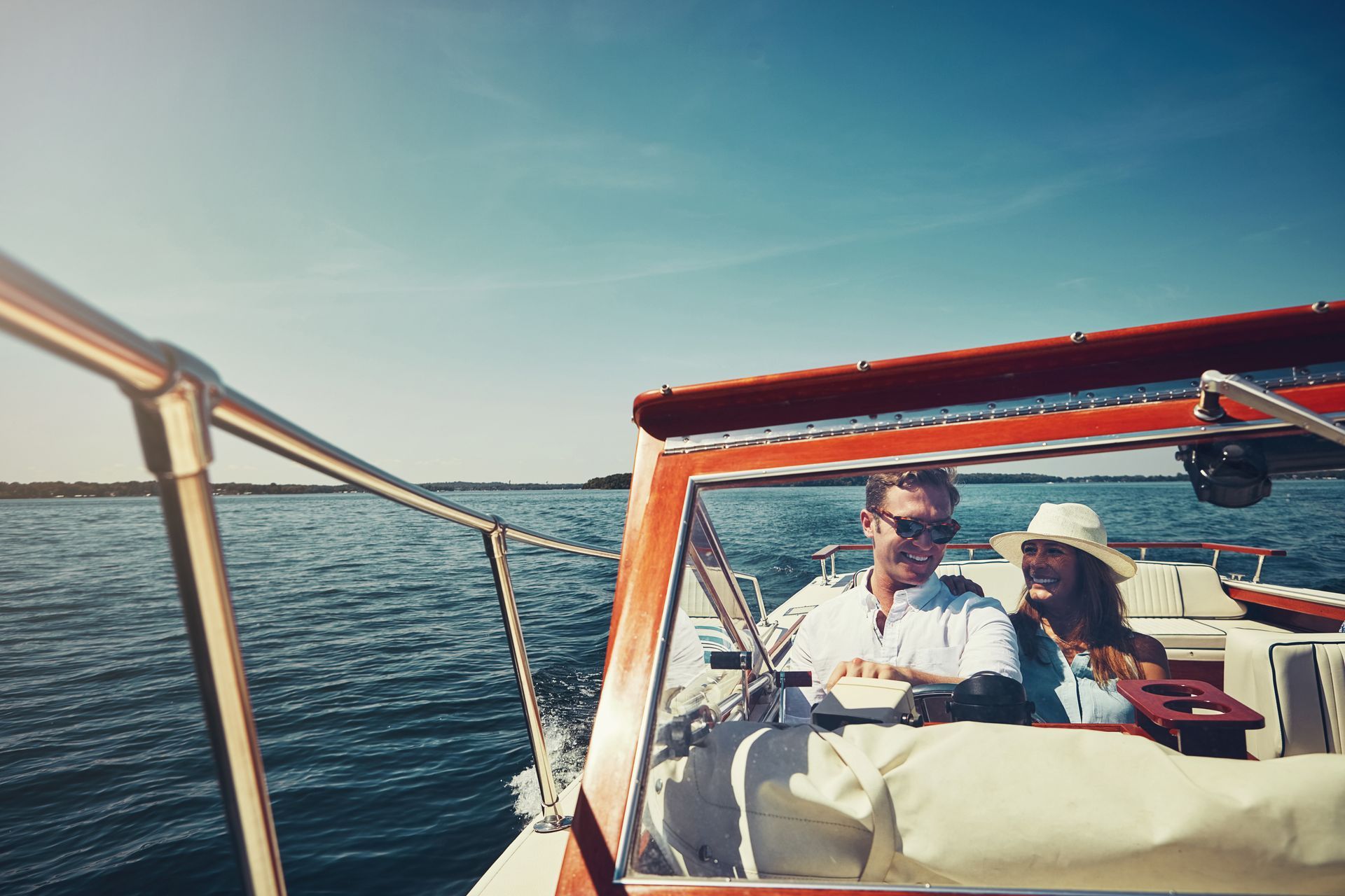 Two people riding in a small red boat on calm water under a blue sky