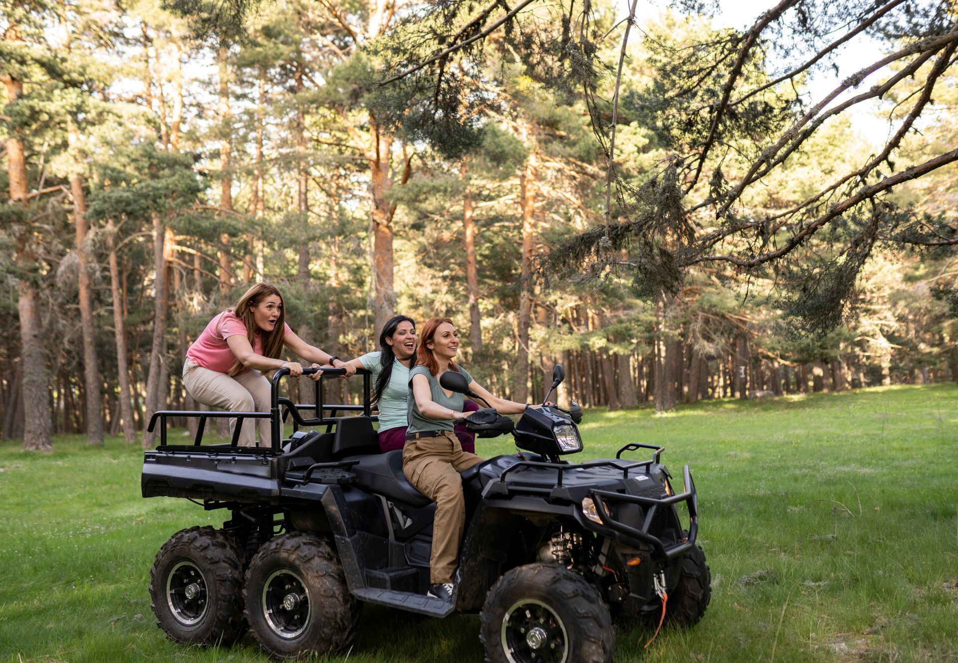 Three people riding an ATV through a grassy forest clearing