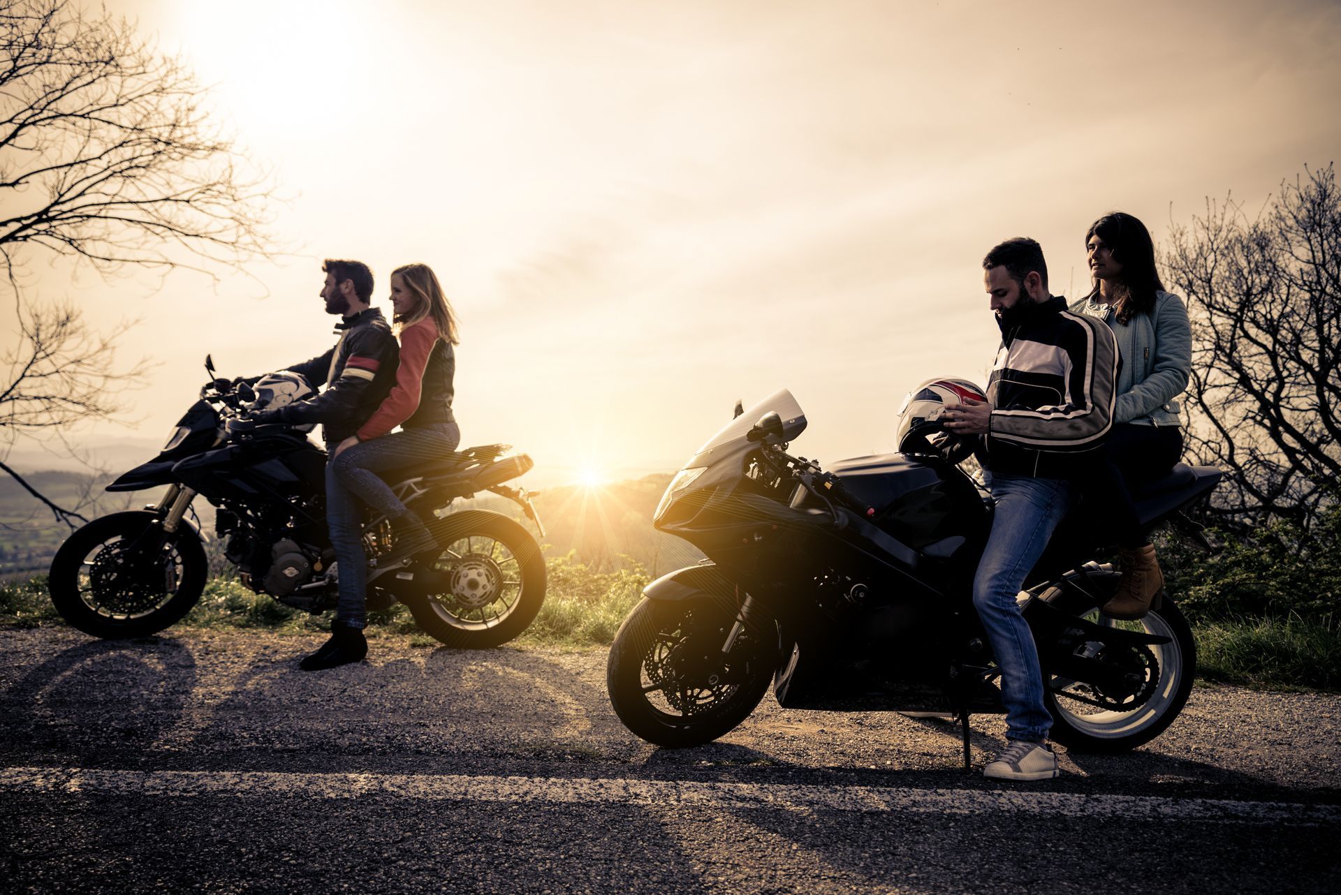 Two motorcycles with riders silhouetted at sunset on a rural road