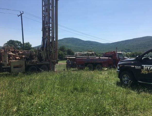 Drilling rig and trucks in a field with mountain backdrop. Sunny day.