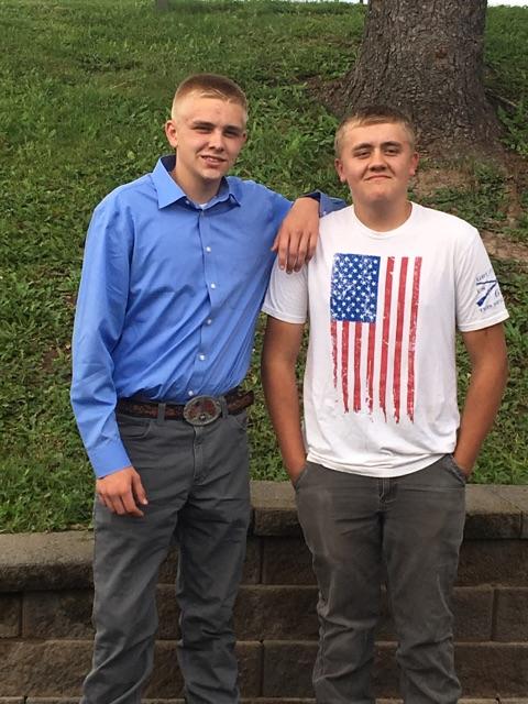 Two young men, one in blue shirt, other in American flag t-shirt, standing outside.