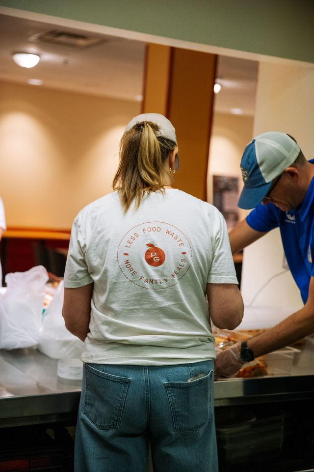 Two people in caps and casual clothes work together at a stainless steel table, preparing items for service.