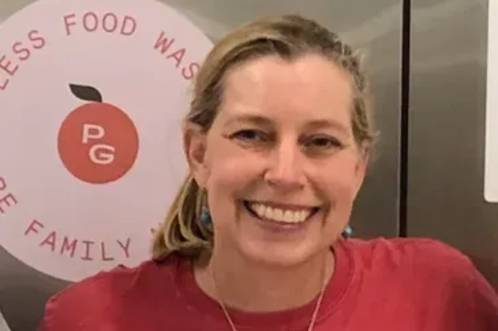A smiling person in a red shirt standing in front of a circular logo with a peach graphic and the text 