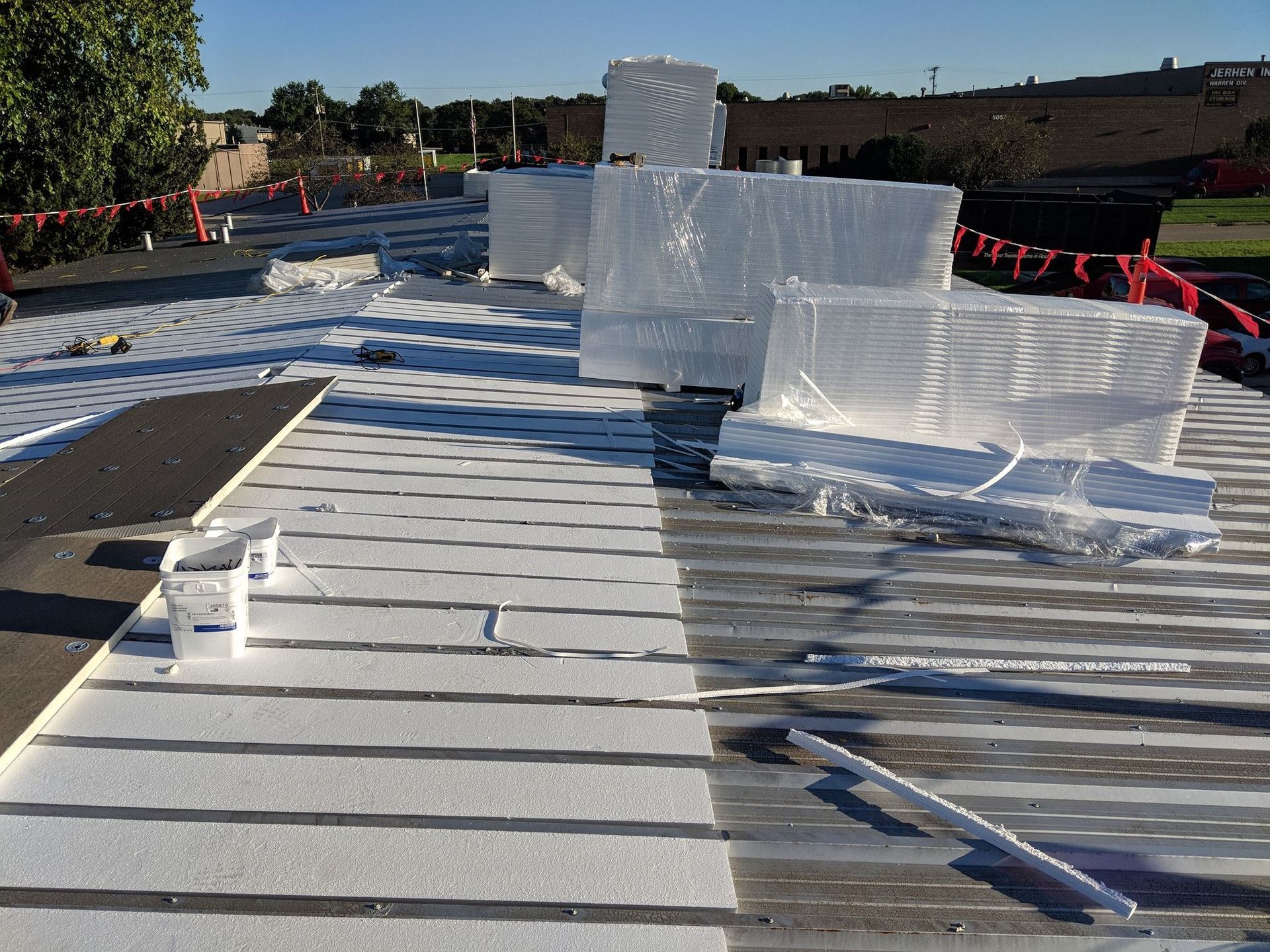 A flat commercial roof under construction with rows of white insulation board and large stacks of wrapped material.