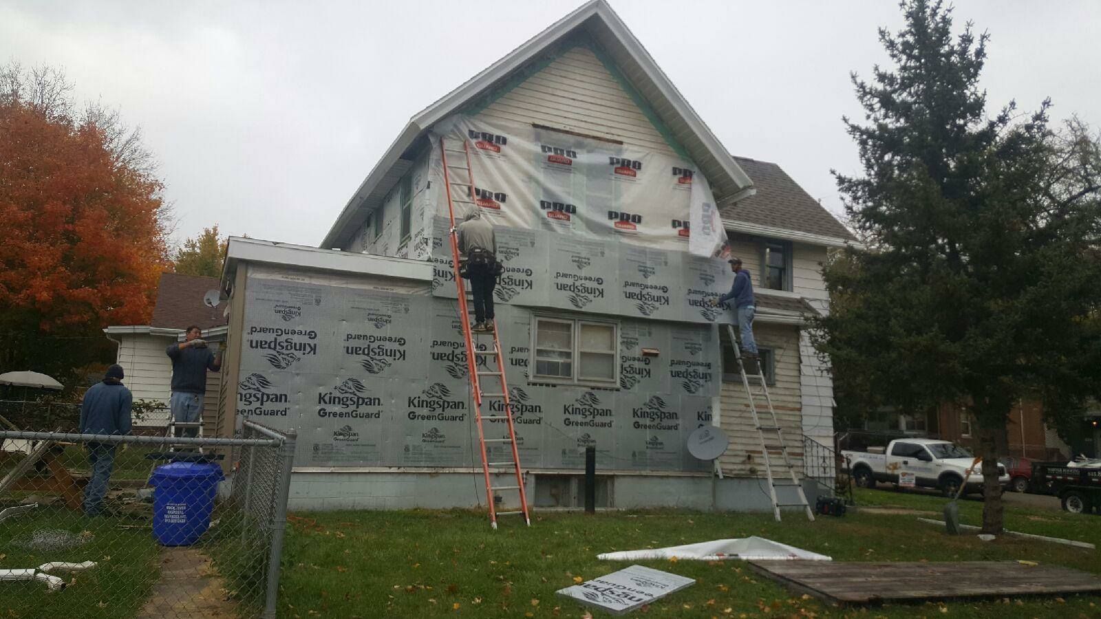 Construction workers on ladders installing weather-resistant barrier house wrap on the exterior of a two-story home.