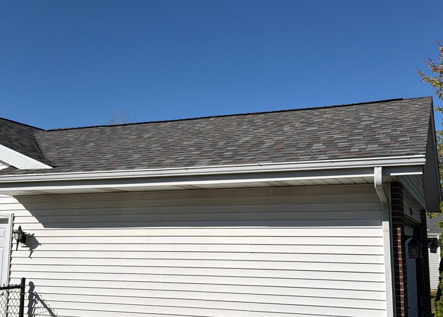 A view of a house exterior featuring a gray shingled roof, white horizontal siding, and a gutter against a blue sky.