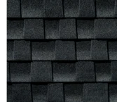 A close-up of dark gray asphalt roof shingles layered in a repeating, overlapping rectangular pattern.
