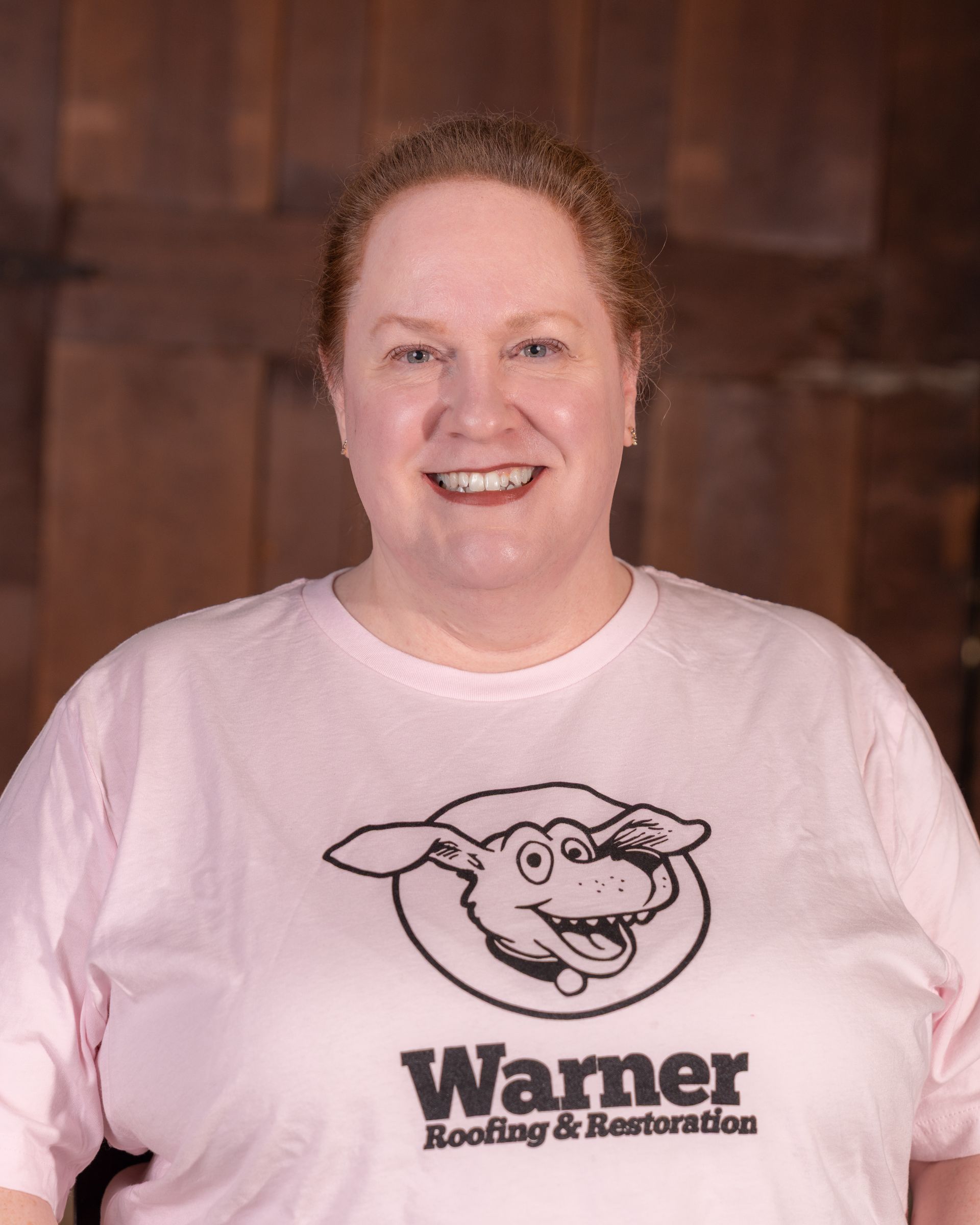A person smiling, wearing a light pink T-shirt featuring a cartoon dog logo and the text 