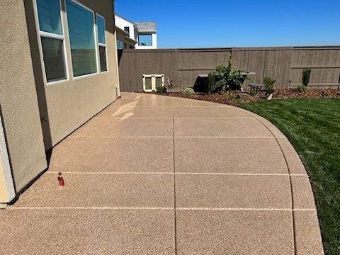 A concrete patio with a fence in the background and a house in the background.