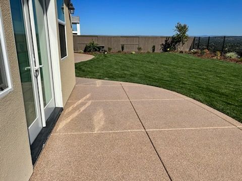 A concrete walkway leading to a house with a large lawn in the background.