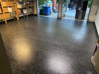 A room with a black floor and a refrigerator in the background.