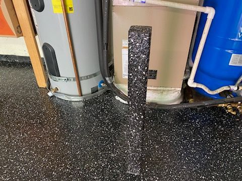 A water heater is sitting next to a blue tank in a garage.