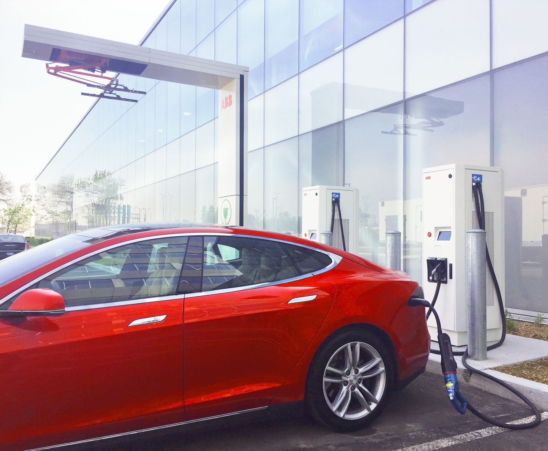 Red electric car plugged into a charging station at a modern outdoor charging area.