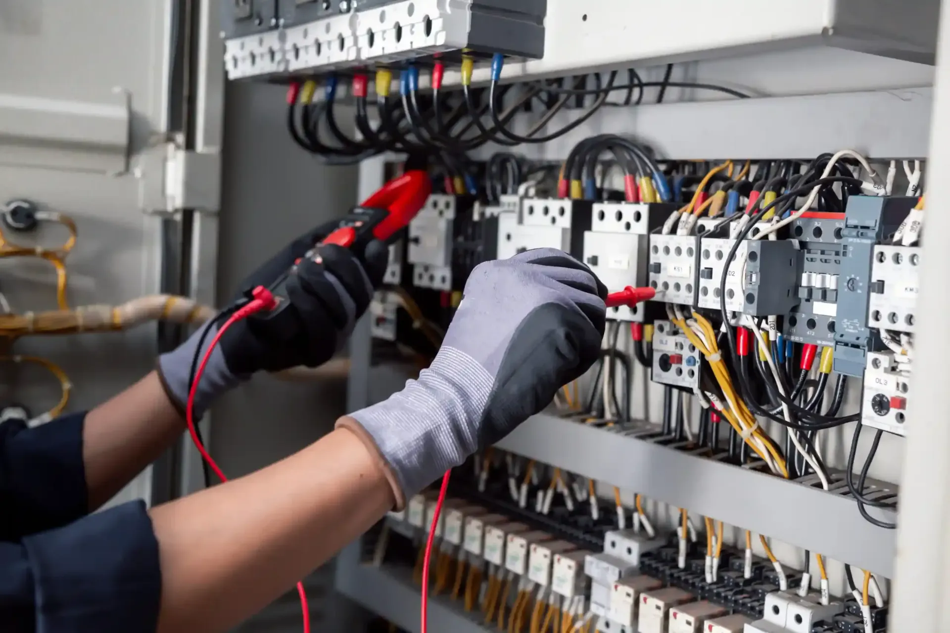 Technician using a red multimeter probe to inspect wiring inside an electrical control panel