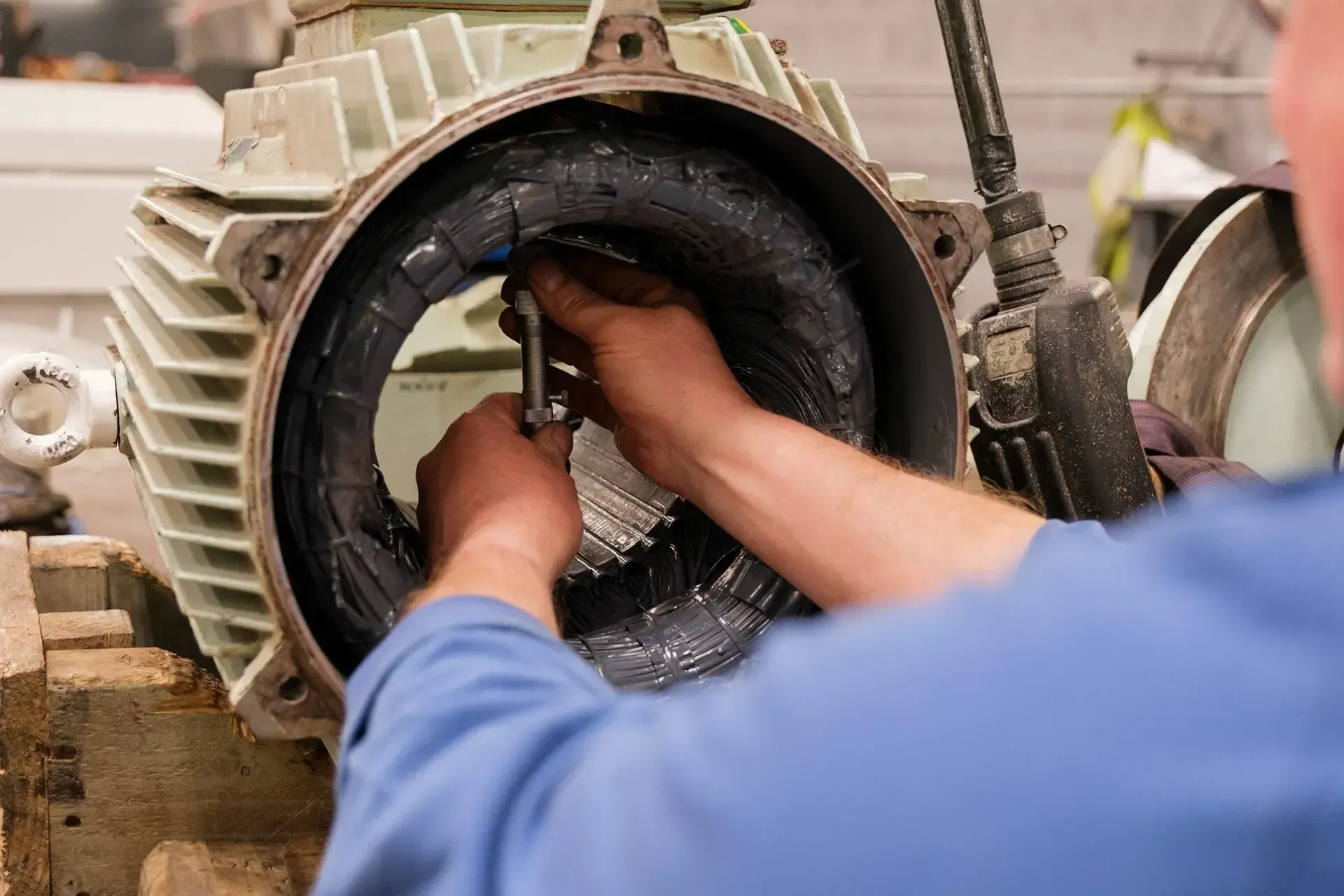 Hands working inside a large industrial pipe or machine opening during maintenance.