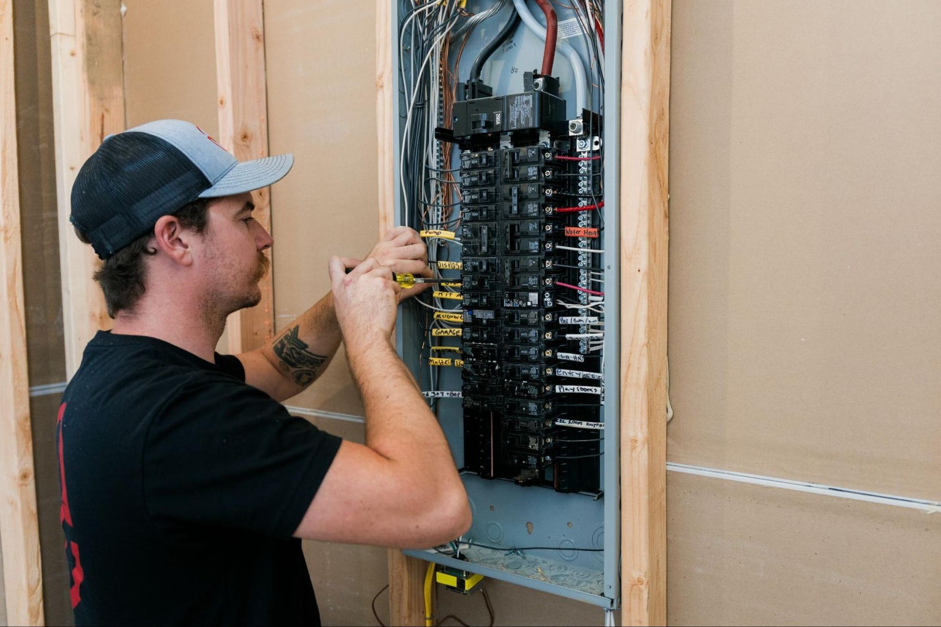 Technician wiring a circuit breaker panel inside a wall-mounted electrical box