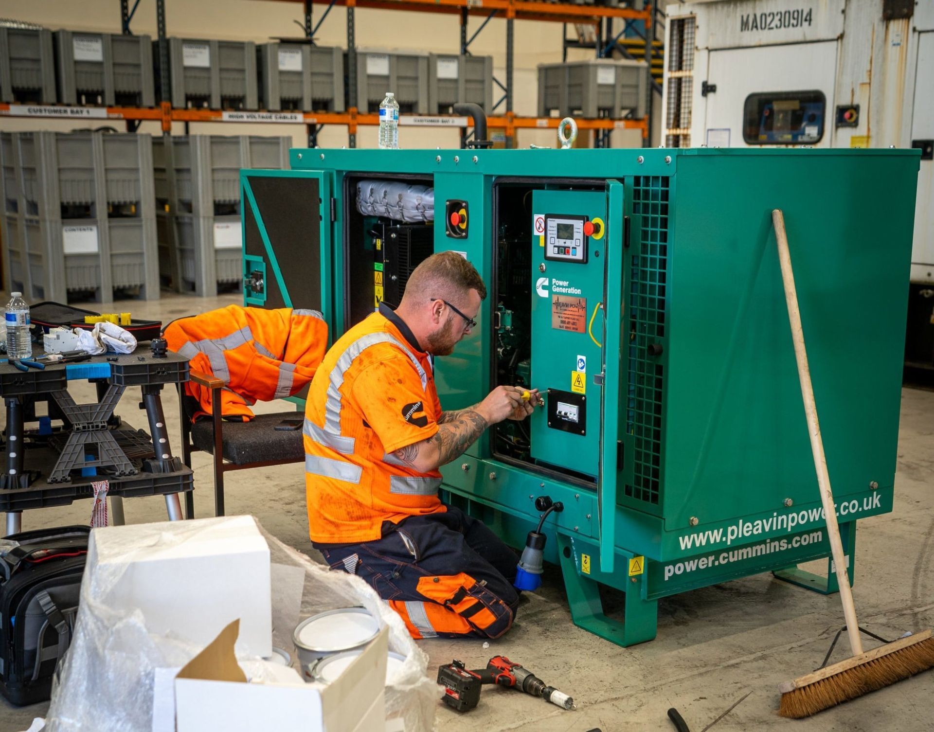 Workers in orange safety gear servicing a large green generator in a workshop