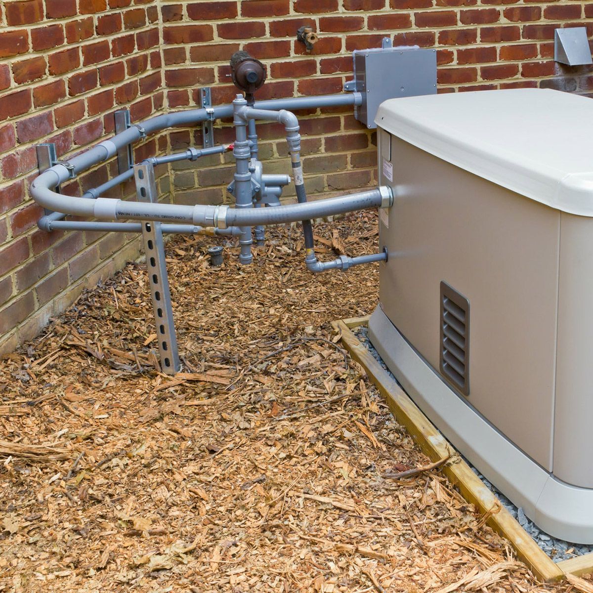 Outdoor utility equipment with gray pipes and valves beside a beige generator, against a brick wall.