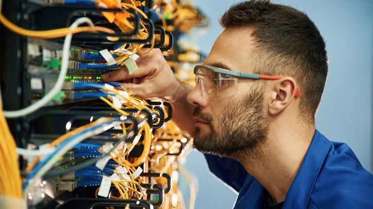 Technician in blue shirt inspecting tangled network cables in a server rack