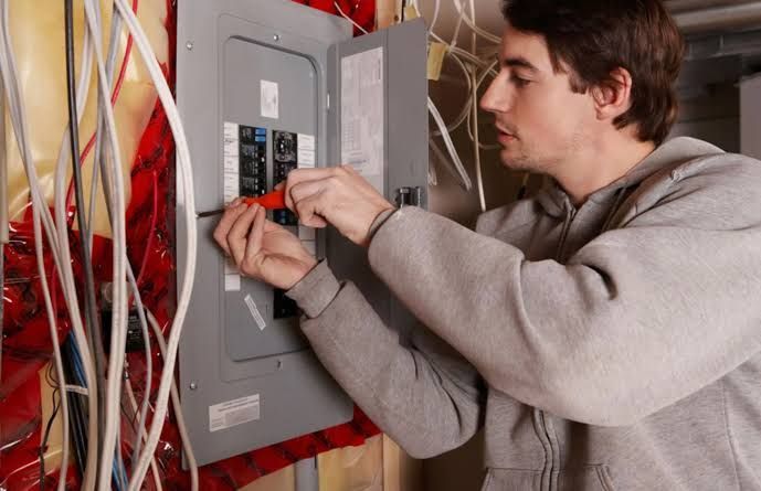 Electrician working on an open electrical panel with exposed wiring.