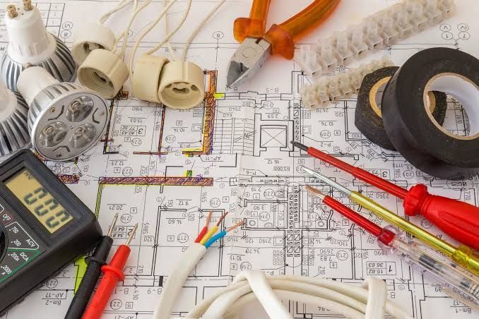 Electrical tools and drafting supplies on a floor plan, including tape, wires, and a multimeter.