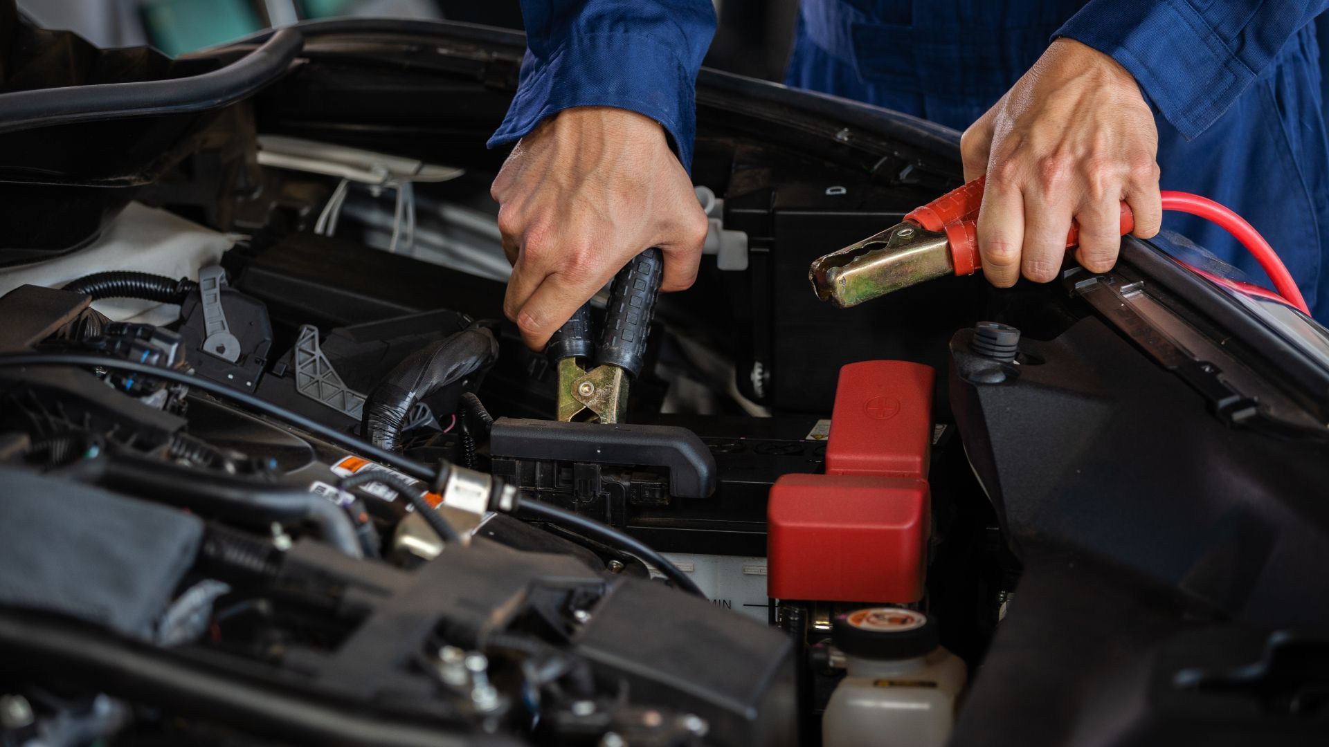 Mechanic using a jumper cable on a car battery in an engine bay