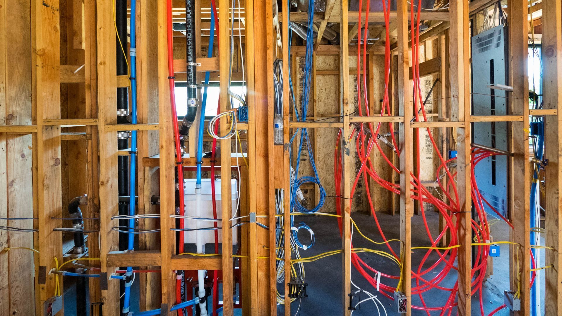 Exposed wall framing with electrical wires and plumbing in an unfinished room under construction
