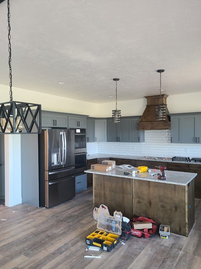 Modern kitchen with gray cabinets, stainless appliances, island, pendant lights, and tools on the floor under construction