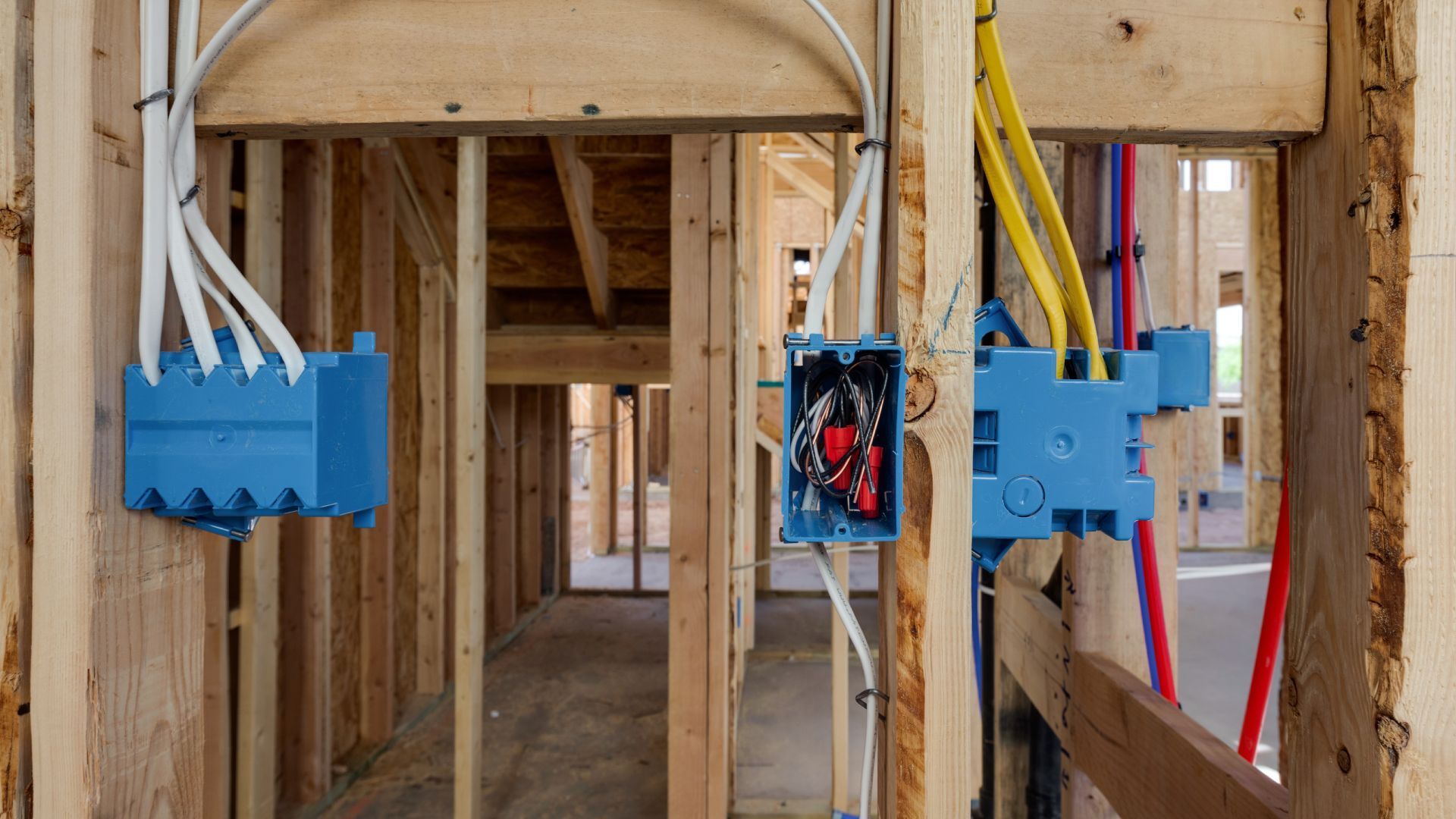 Interior wall framing with blue electrical boxes and wiring in a house under construction