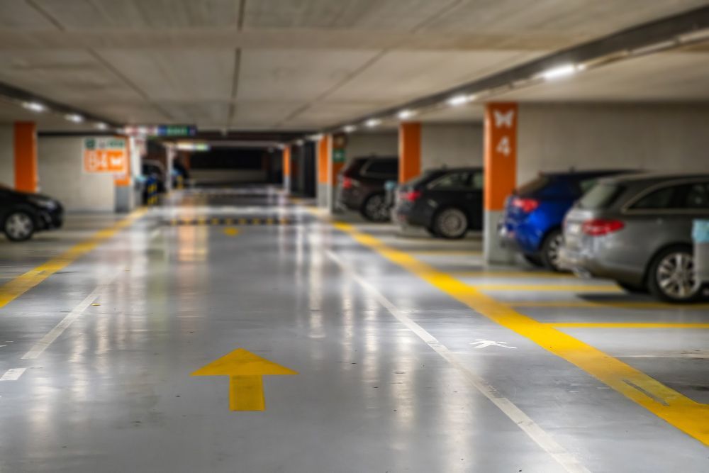 Estacionamento coberto com carros estacionados em ambos os lados e uma seta amarela no chão.