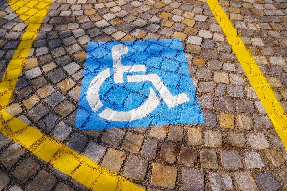 Símbolo azul de acessibilidade para cadeirantes pintado em calçada de paralelepípedos com linhas amarelas.