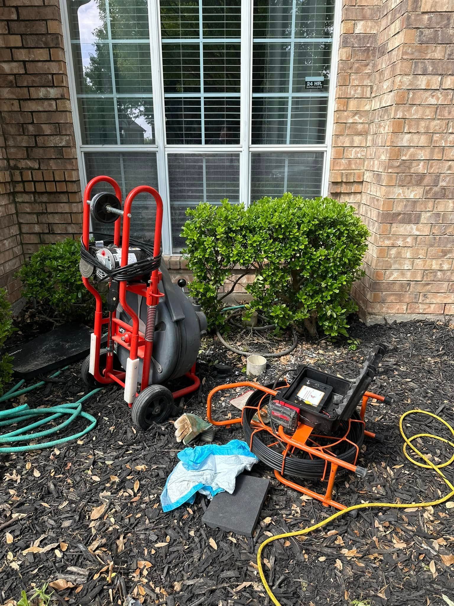 A drain cleaning machine is sitting in front of a brick house.