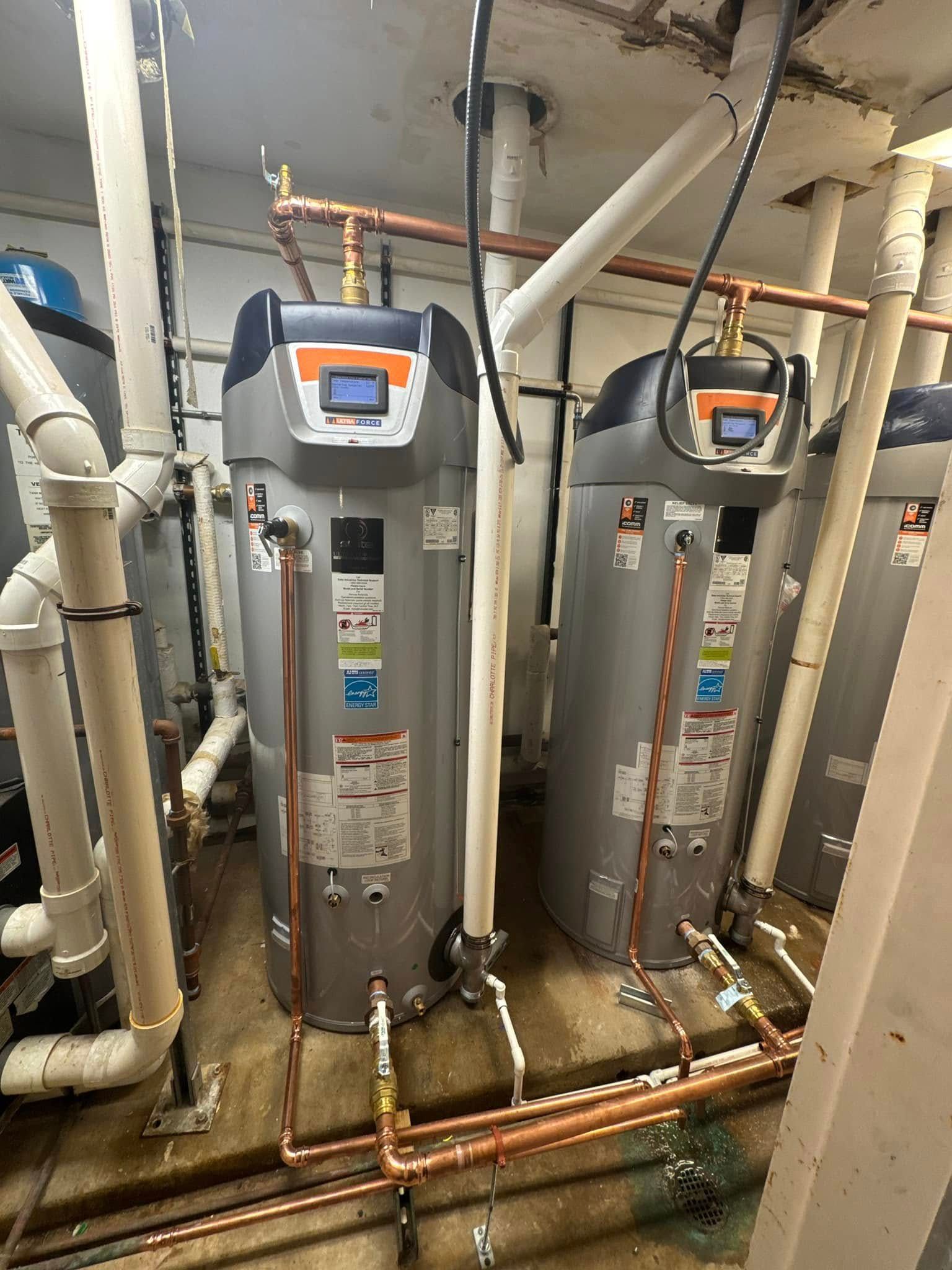 Two water heaters are sitting next to each other in a room with pipes.