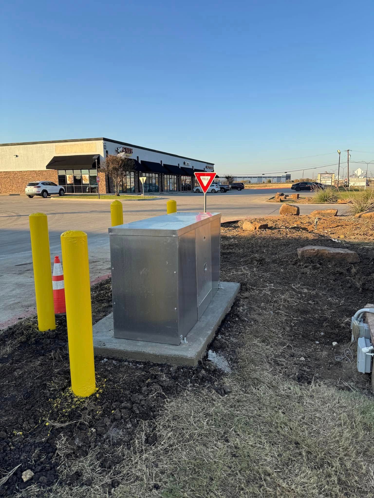 A stainless steel box is sitting in the dirt in front of a building.