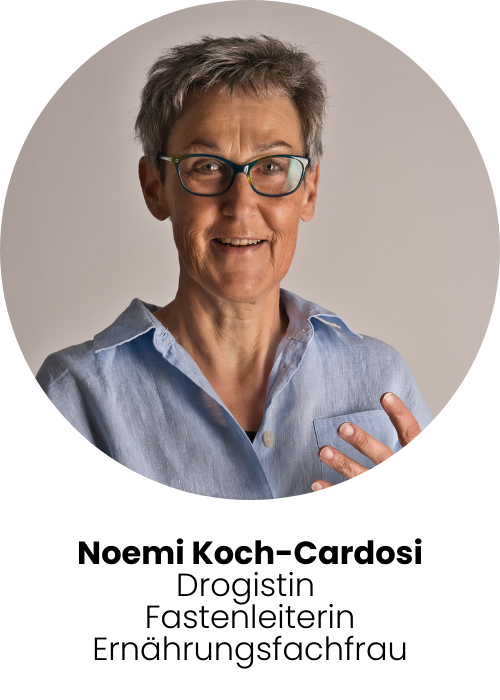 Foto Noemi Koch - Noemi steht vor einem neutralen Hintergrund, sie trägt ein Denimhemd. Noemi hat kurze Haare und trägt eine Brille.