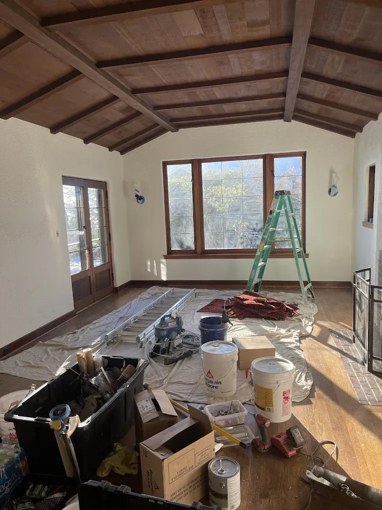 A living room with a ladder and buckets of paint on the floor.