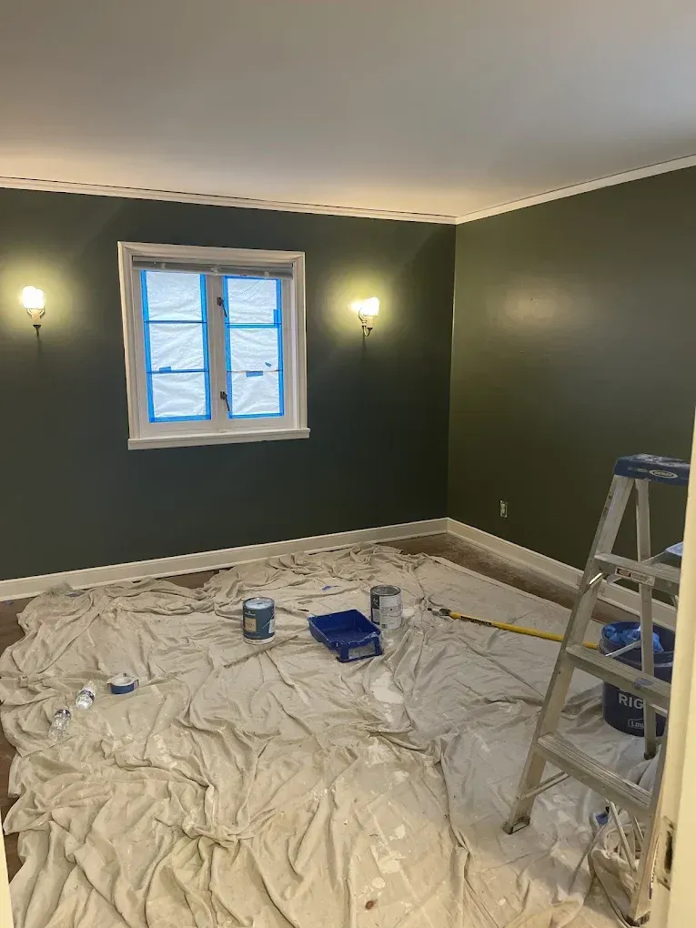 A room with a ladder and a blanket on the floor is being painted.