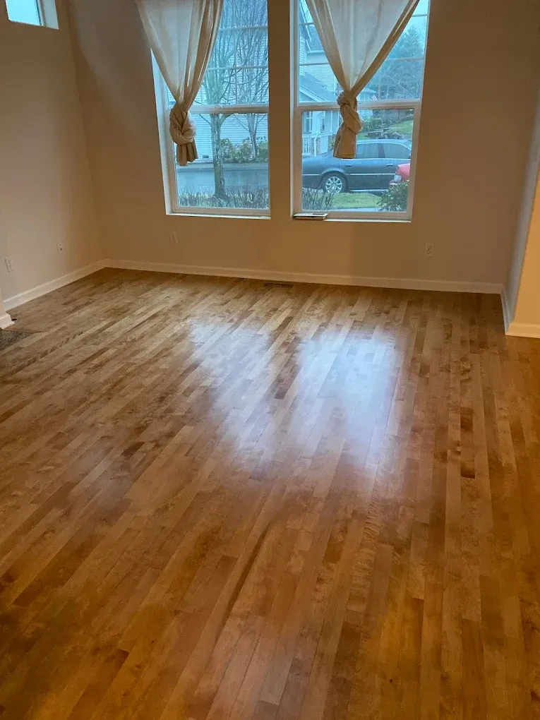 An empty living room with hardwood floors and two windows.