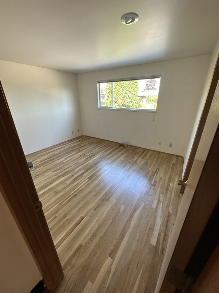A bedroom with hardwood floors and a window.