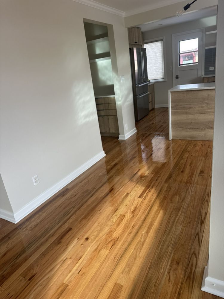 A living room with hardwood floors and a kitchen in the background.