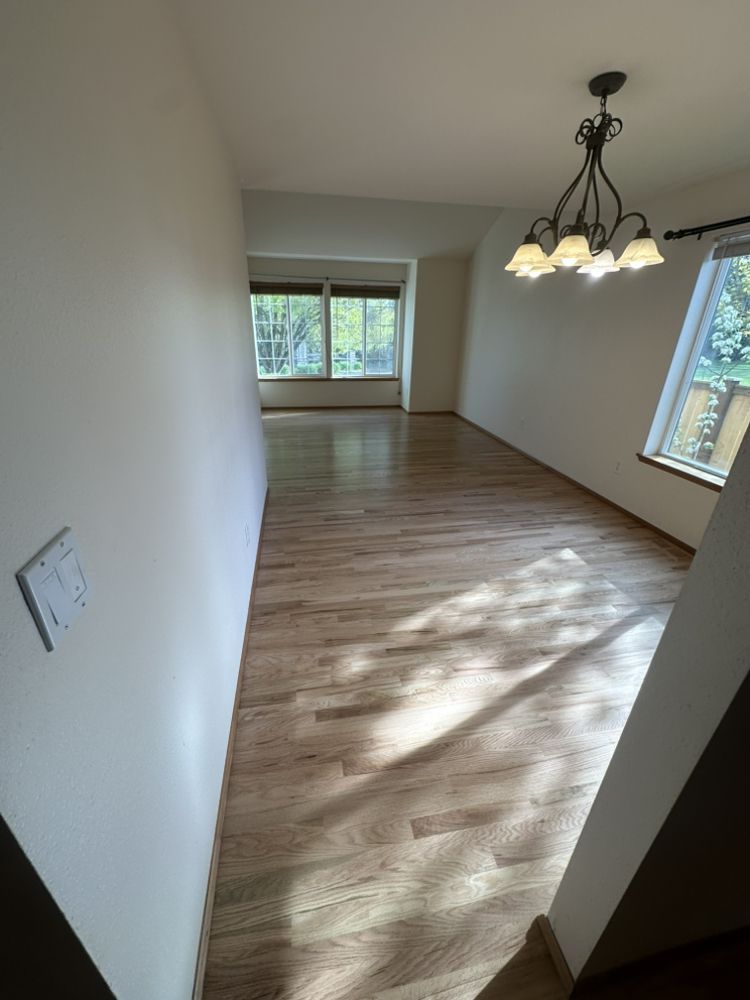 An empty living room with hardwood floors and a chandelier hanging from the ceiling.