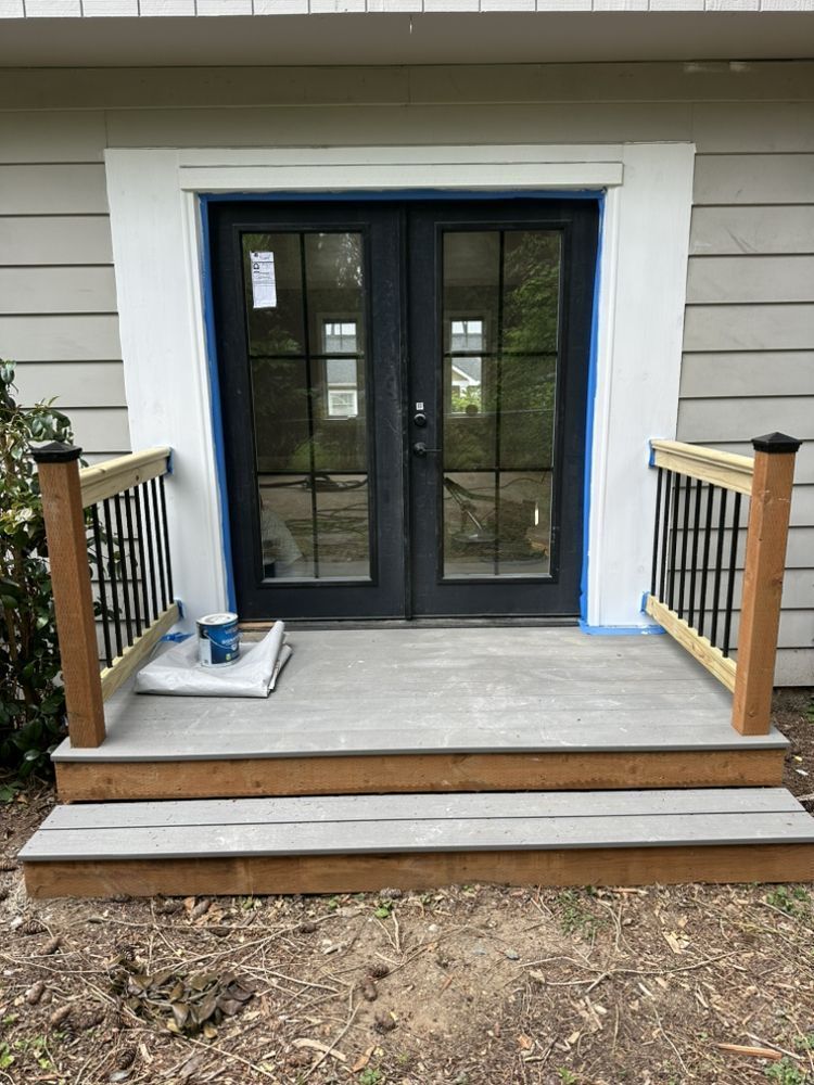 A patio with a wooden railing and sliding glass doors is being built in front of a house.