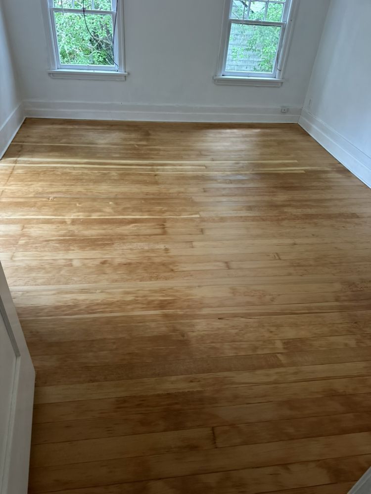 A bedroom with hardwood floors and two windows.