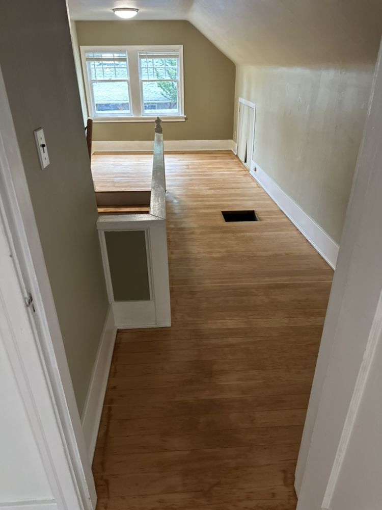 A hallway in a house with hardwood floors and stairs leading to a living room.
