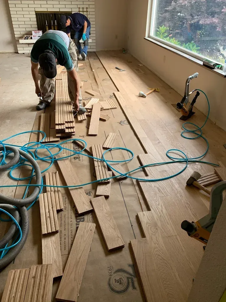Two men are working on a wooden floor in a living room.