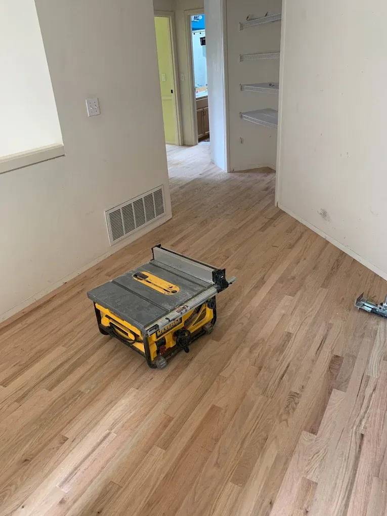 A table saw is sitting on a wooden floor in a room.